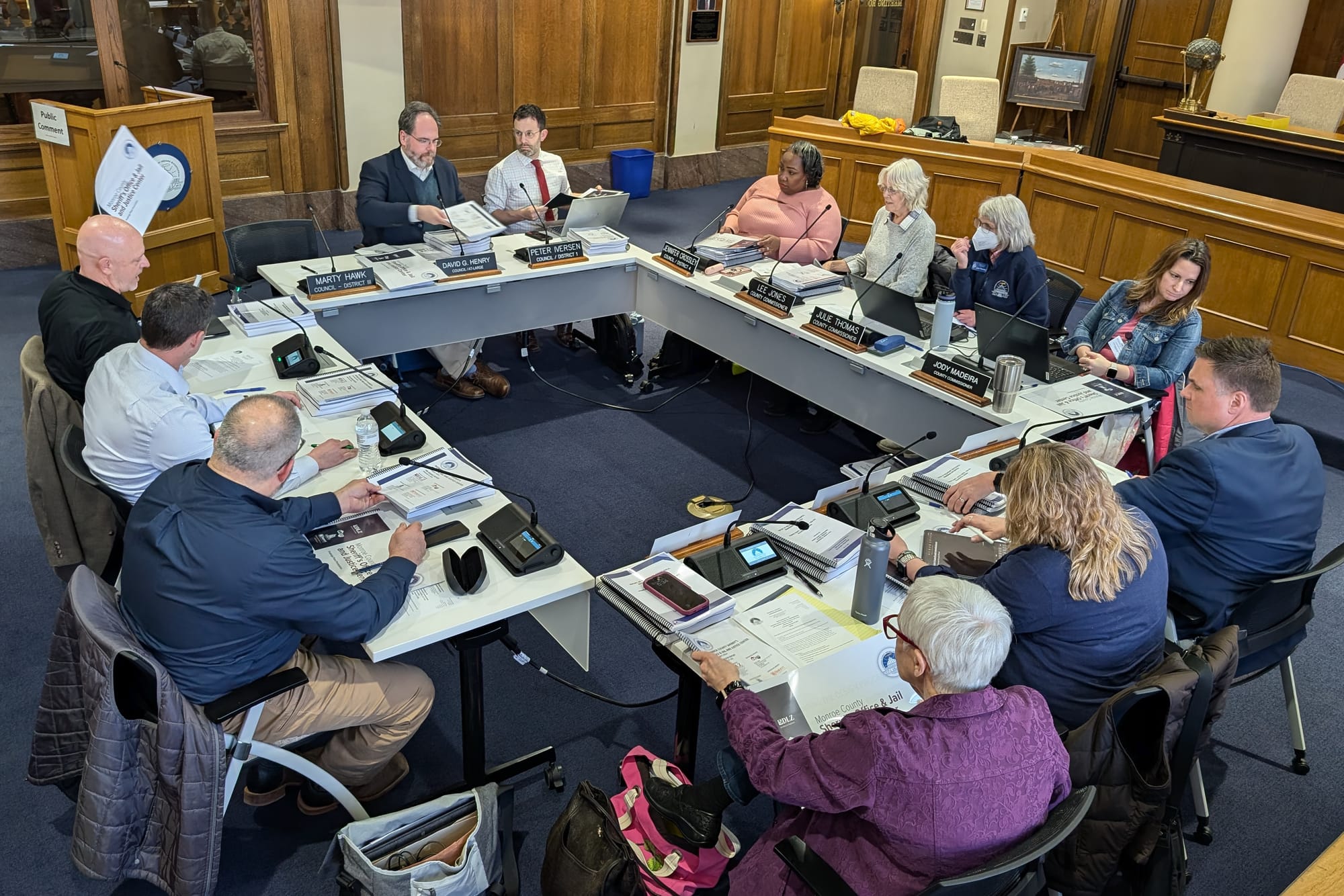 A group of 12 people sitting around a square table. The view is slightly from above.