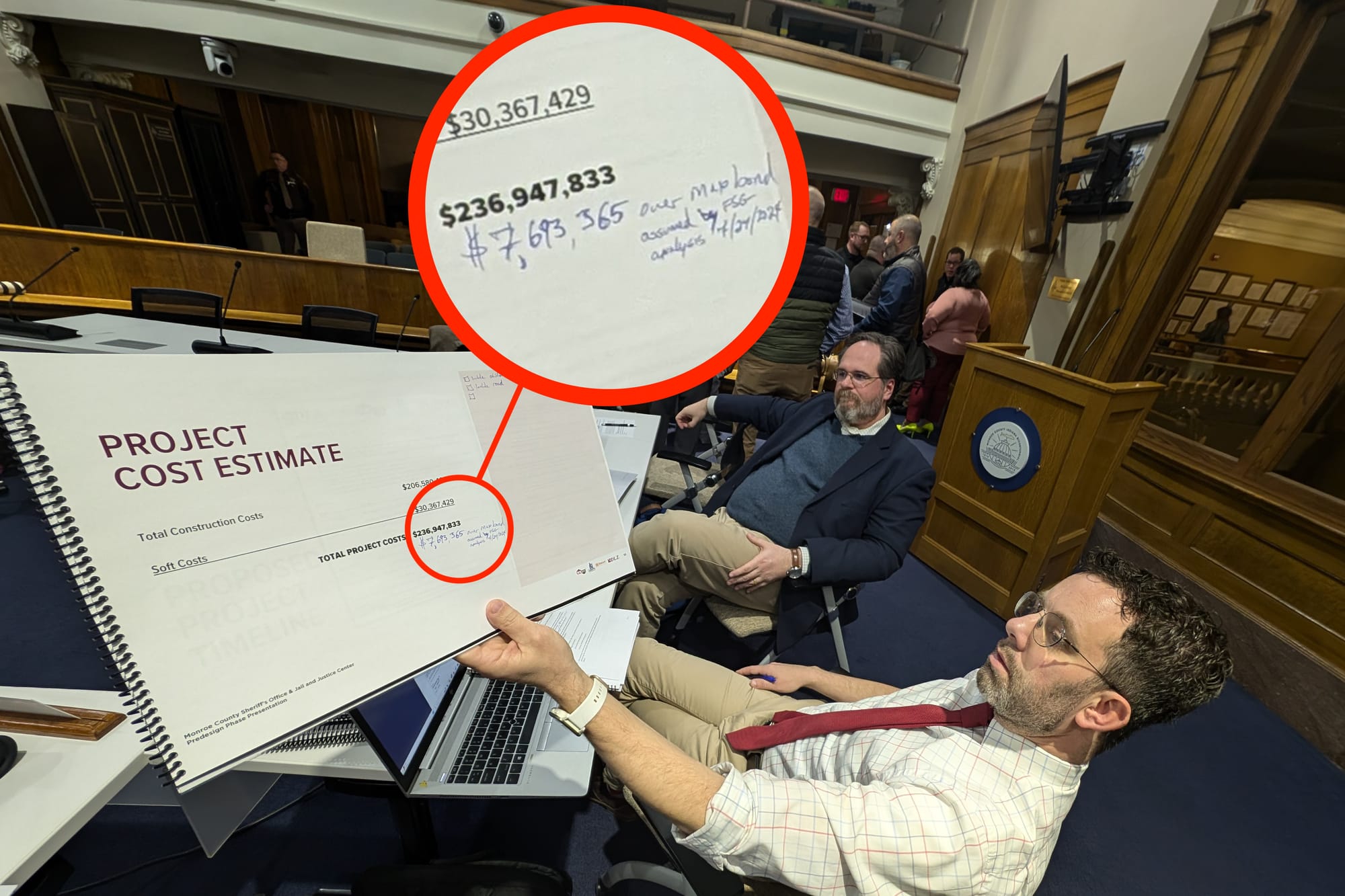 A man sits at a table holding a printed booklet with financial information.