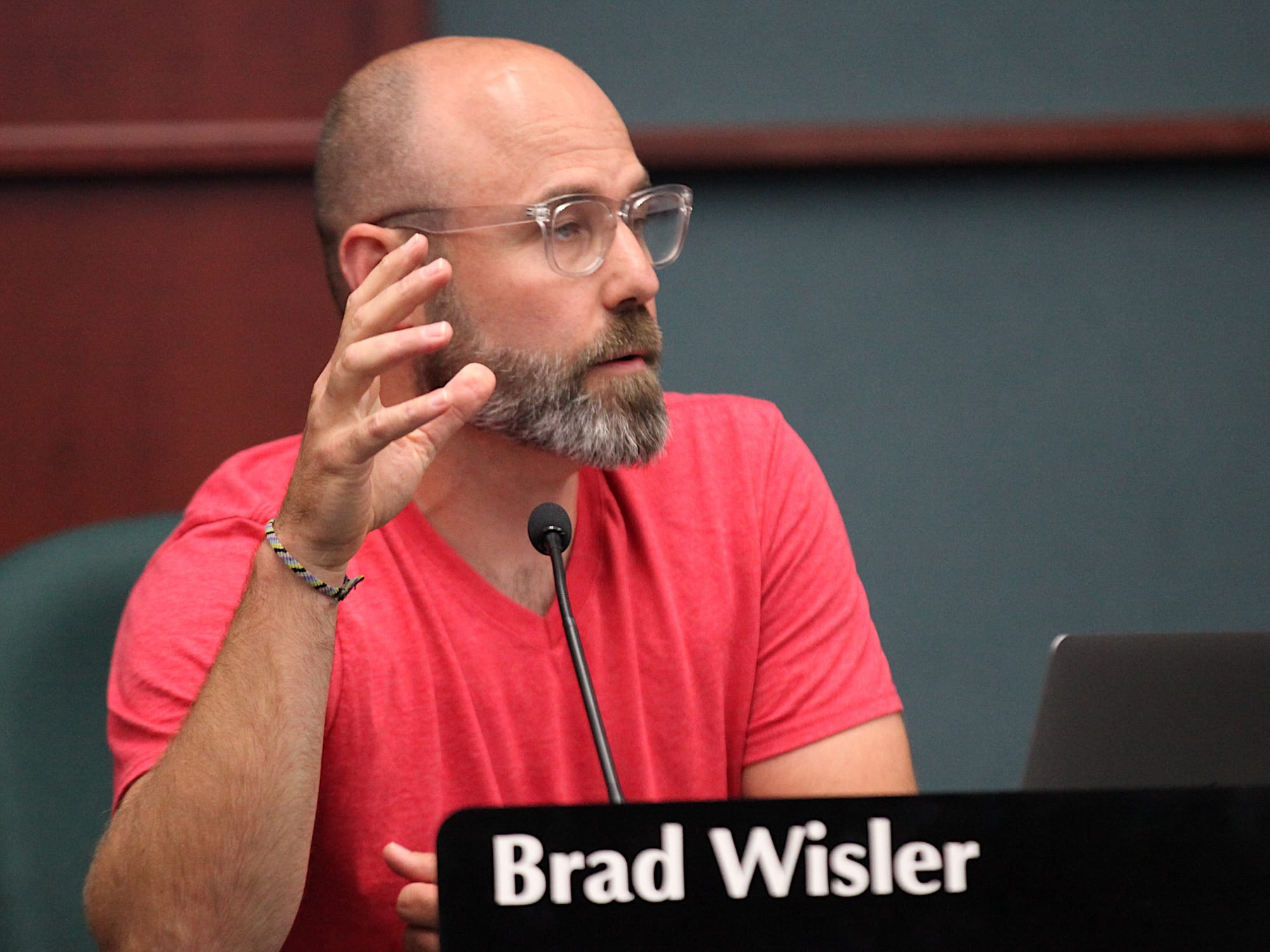 Man sitting at dais speaking in to microphone gesturing with right hand