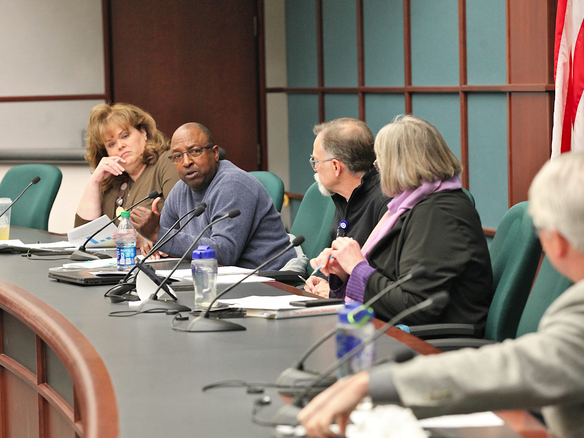 view looking down the city council dais from the right, one councilmember is leaning in looking towards the camera