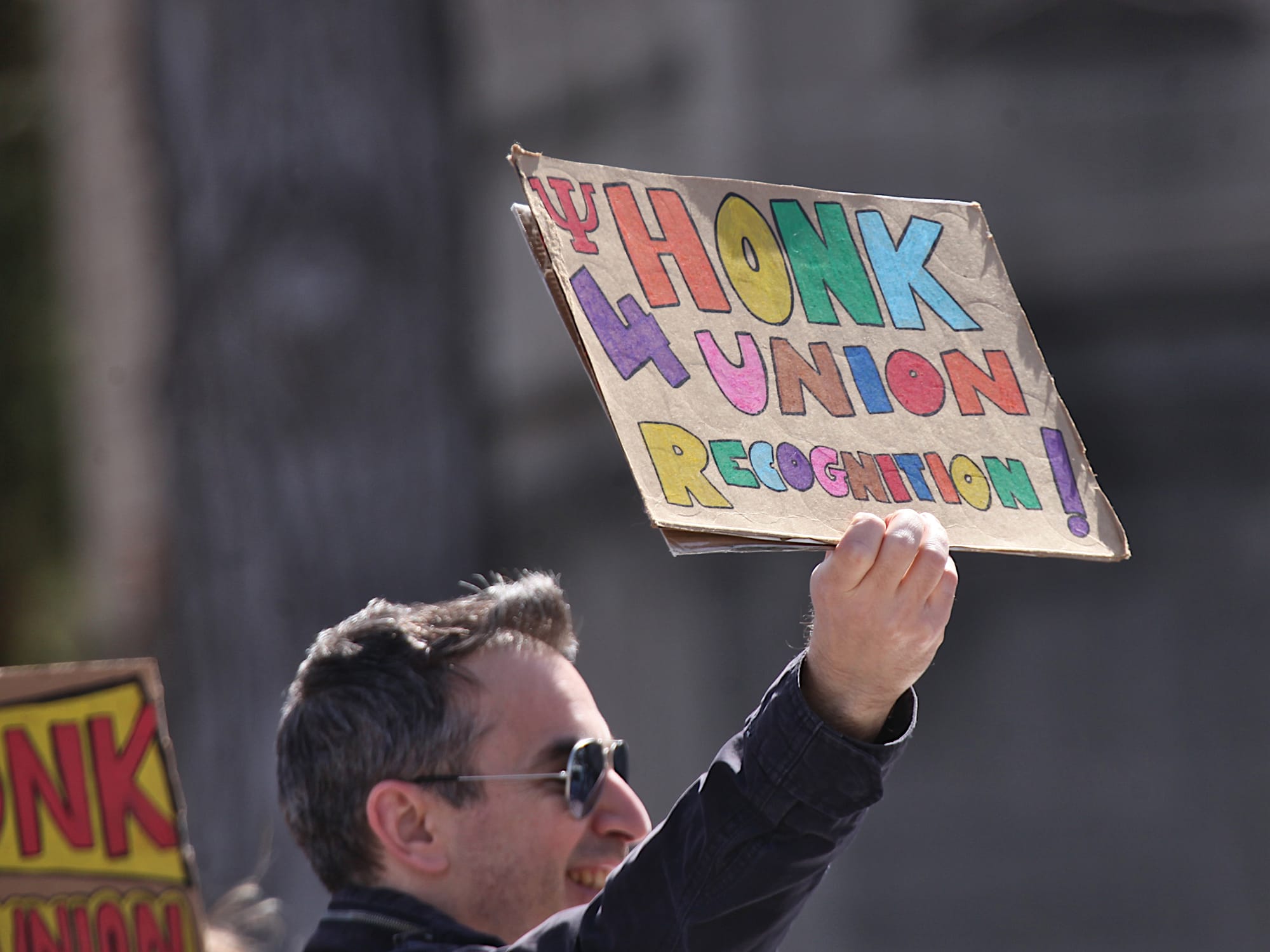 Man holding a cardboard hand-lettered sign that reads "Honk 4 union recognition."