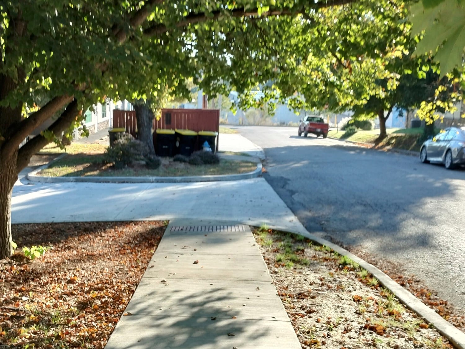 A narrow, concrete sidewalk that ends at a place where a place for dumpsters and trash cans has been installed.